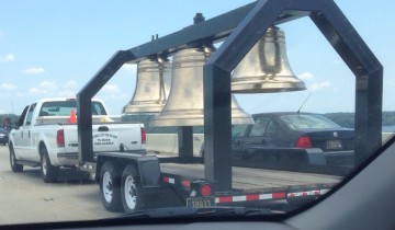 A truck pulling a trailer with 3 church bells on it